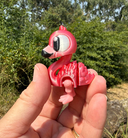 Small pink flamingo 3d printed figurine held in a hand with a blurred green outdoor background