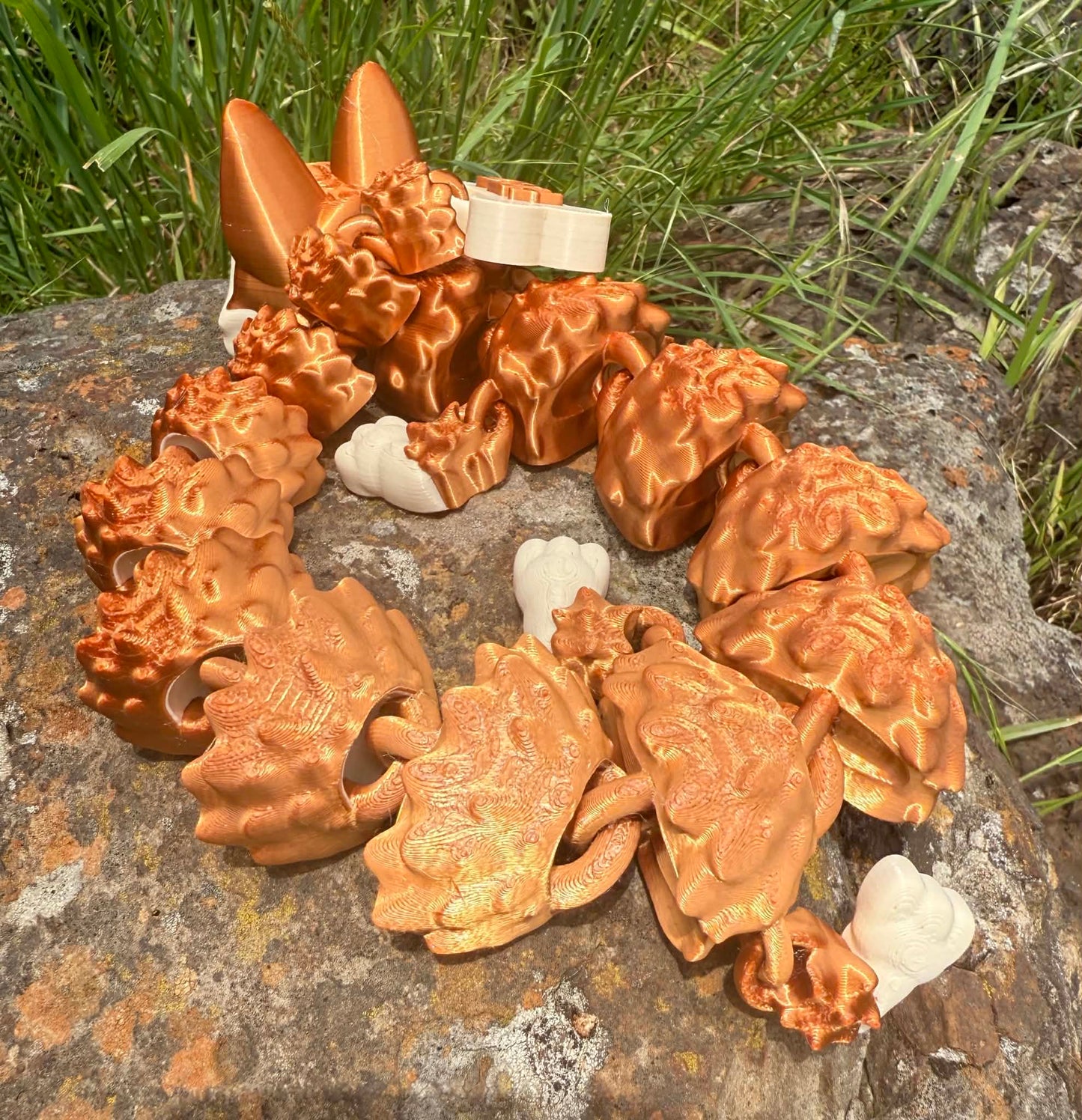 Bronze-colored dragon-shaped German Shepard 3d printed on a stone surface with grass in the background