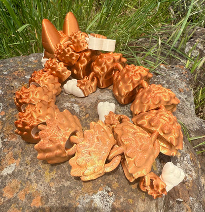 Bronze-colored dragon-shaped German Shepard 3d printed on a stone surface with grass in the background