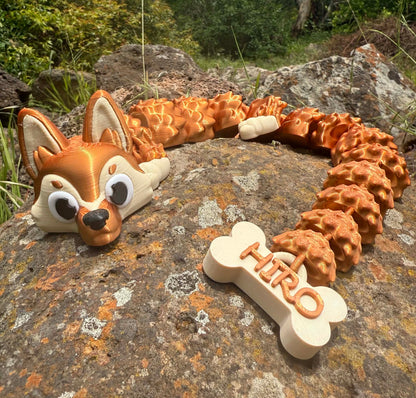 3D printed German Shepard dragon with a bone-shaped tag labeled 'Hiro' on a rocky surface outdoors