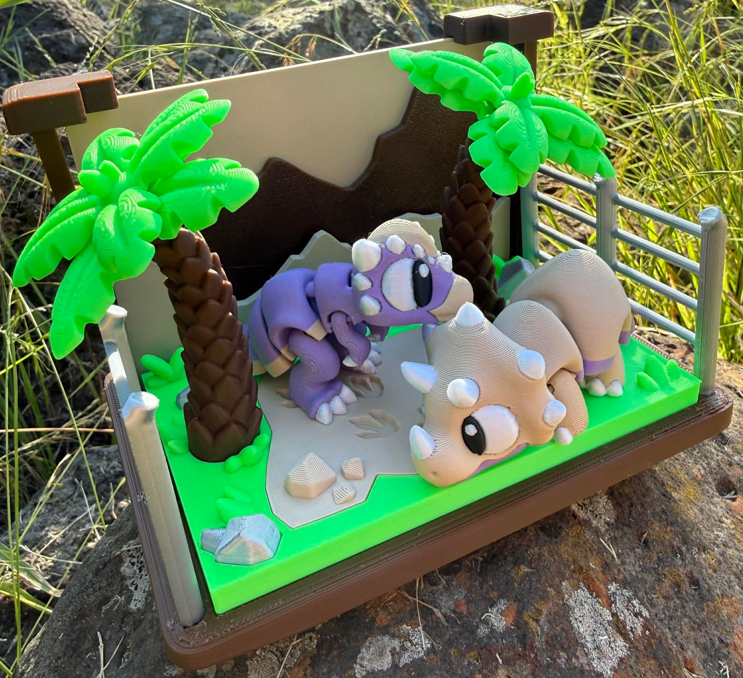 3d printed dinosaurs on a miniature landscape with palm trees and rocks.