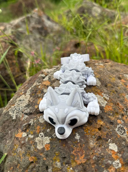 White and silver 3D-pinted Husky dog mini dragon on a textured rock surface with grass in the background