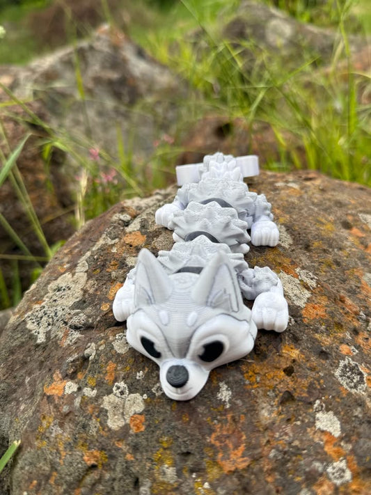 White and silver 3D-pinted Husky dog mini dragon on a textured rock surface with grass in the background
