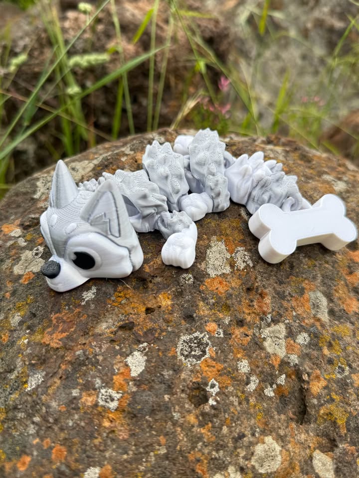 Gray and white 3d printed Husky dog dragon on a textured rock surface with grass in the background