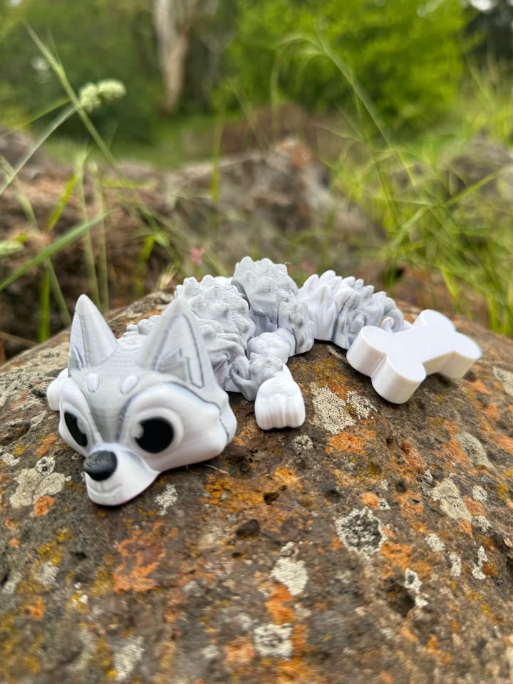 White and grey Husky dragon 3d printed on a textured rock surface with greenery in the background