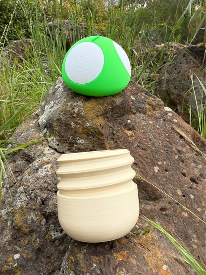 Green and white spherical 3d printed moneybox lid on a rock with a beige 3d printed screw bottom of the moneybox