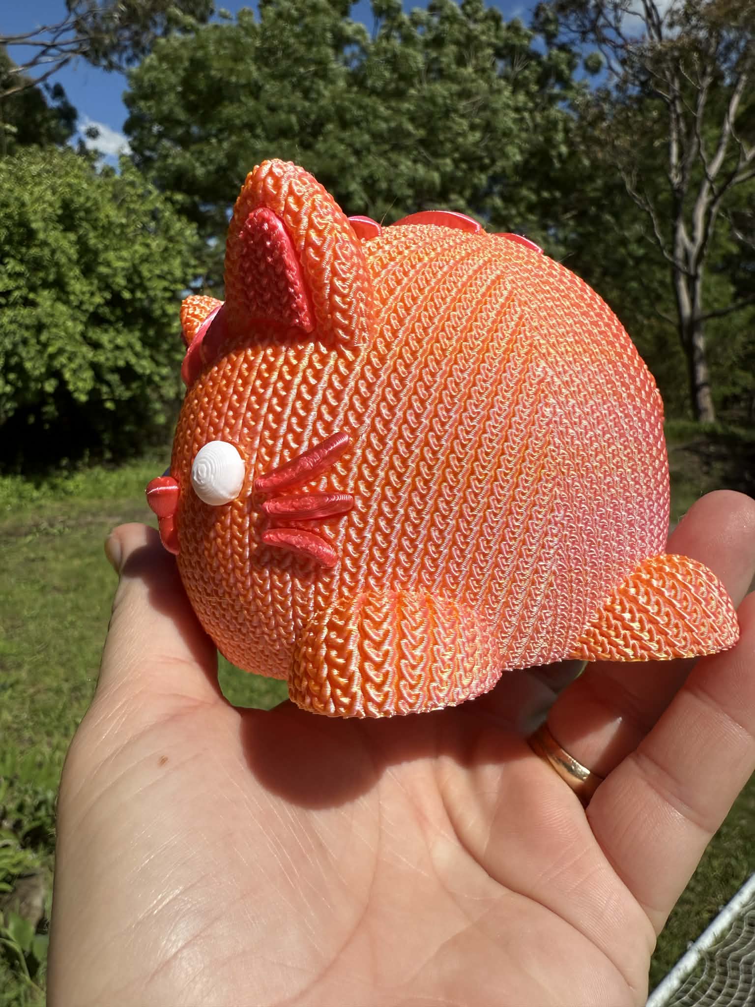 Hand holding a knitted orange cat money box 3d printed with a blurred natural background