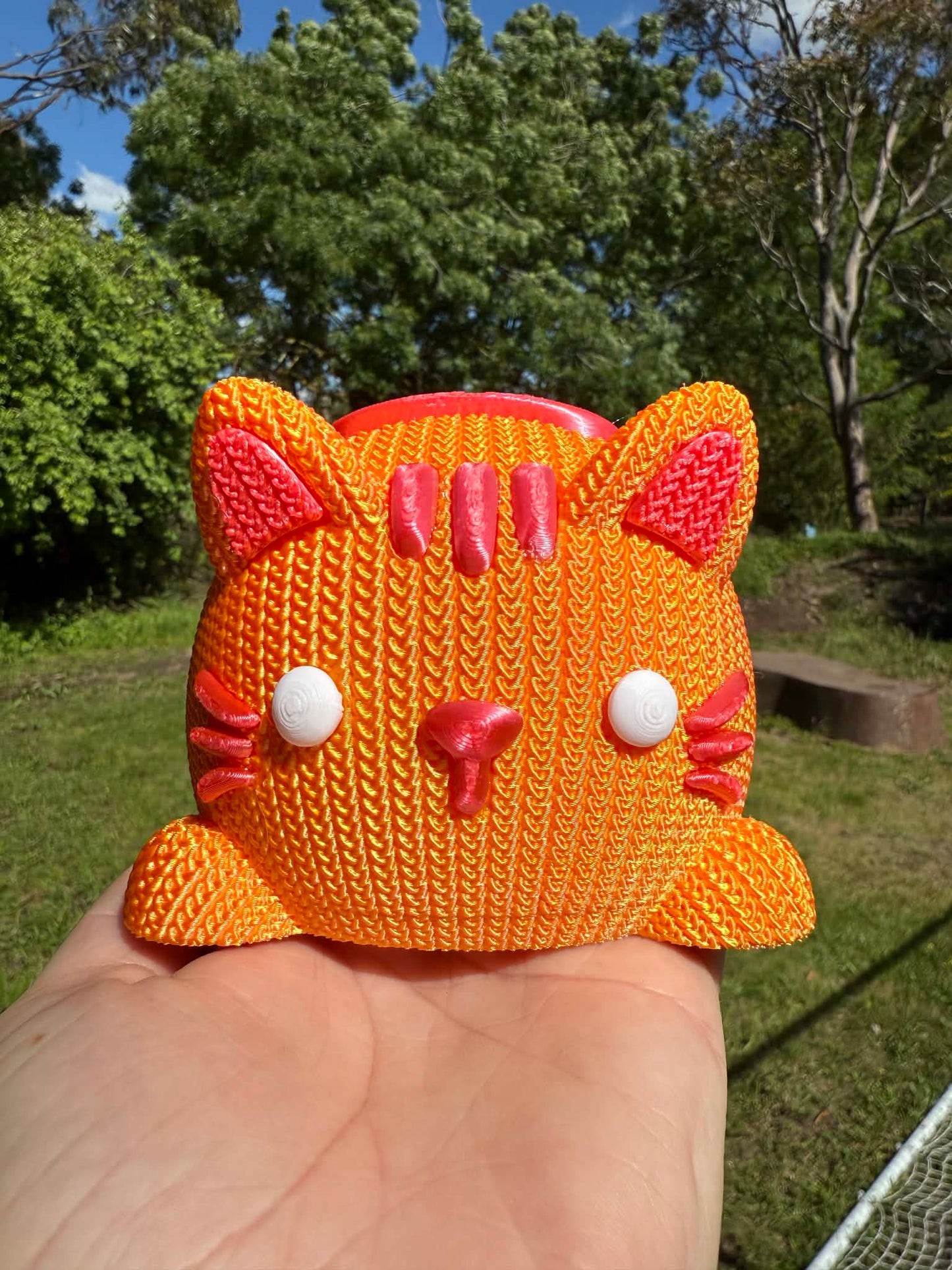 Orange and pink Knitted cat money box 3D printed held in a hand with a natural background