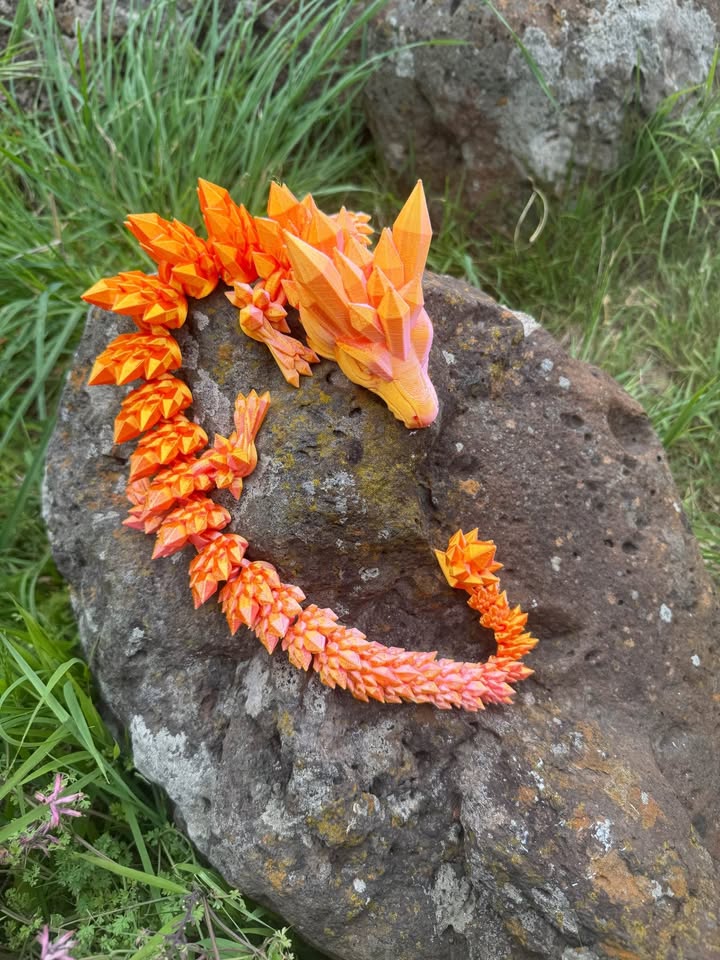 Orange dragon 3d printed on a rock with grass and rocks in the background