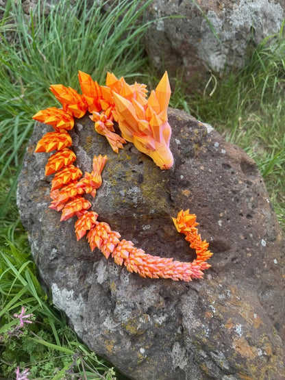 Orange dragon 3d printed on a rock with grass and rocks in the background
