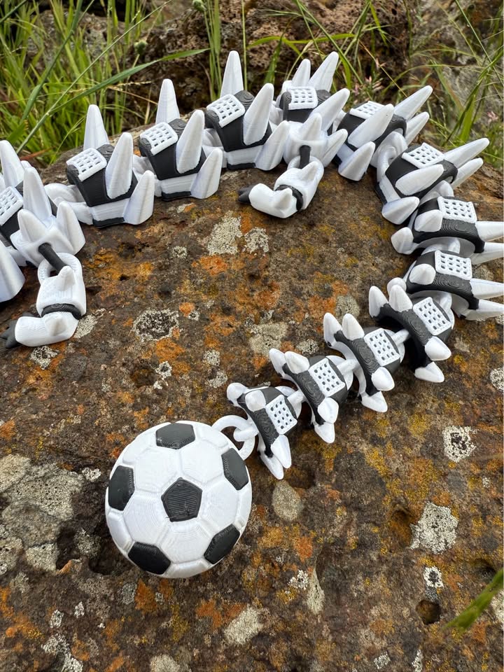 Black and white 3d printed dragon with a soccer ball head on a textured surface