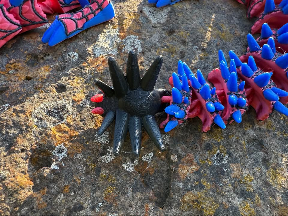 3d printed dragon tail with black spider with red eyes on the tail of the dragon on a textured stone surface