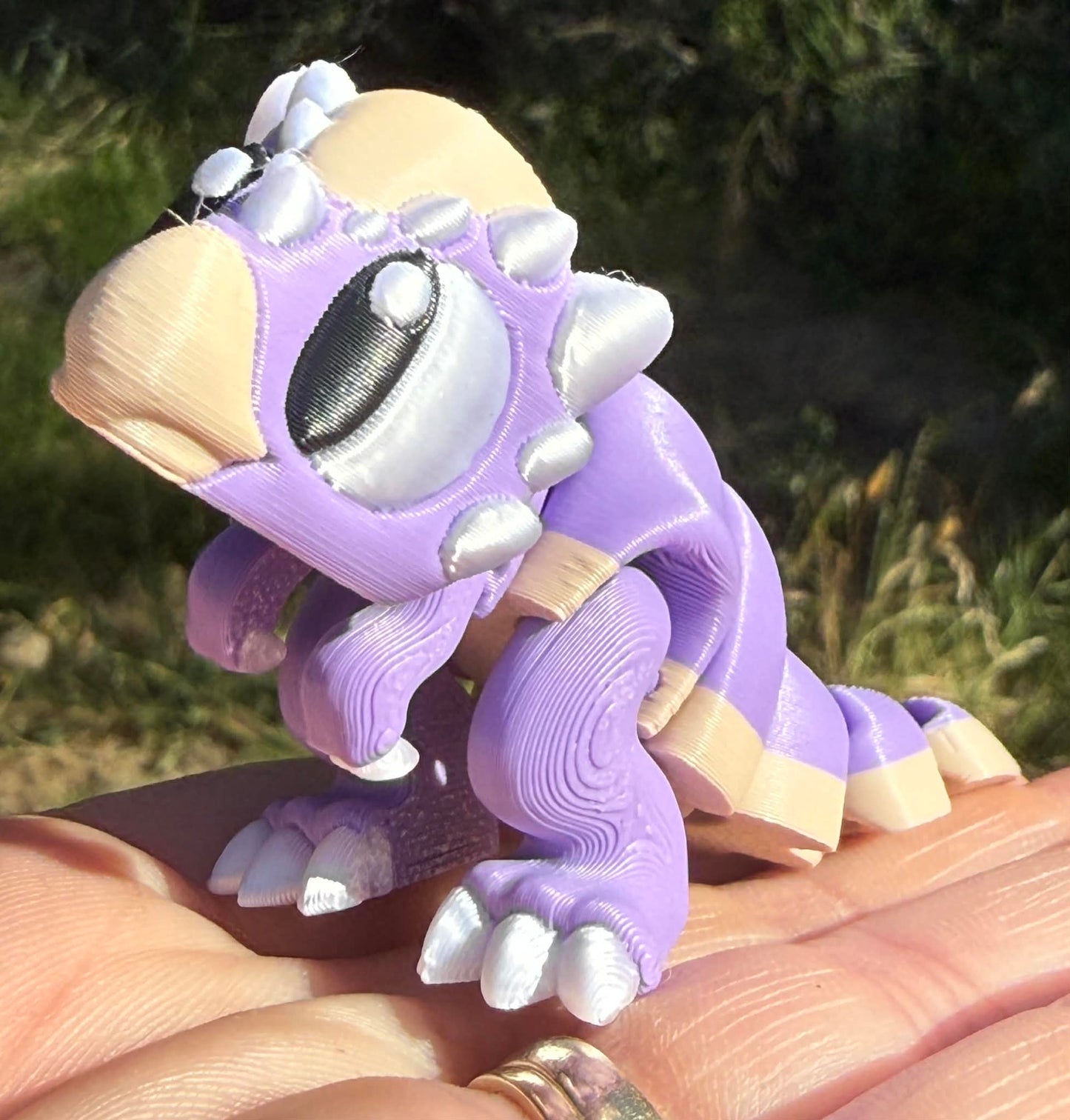 Purple and beige dino 3d printed figurine held in a hand with a natural background