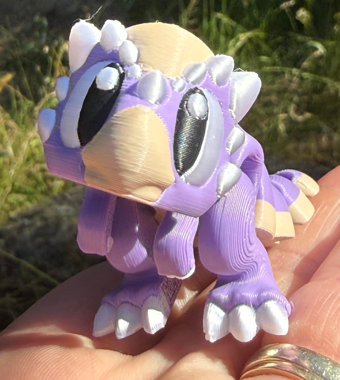 Purple and beige 3d printed dino figure held in a hand with a natural background