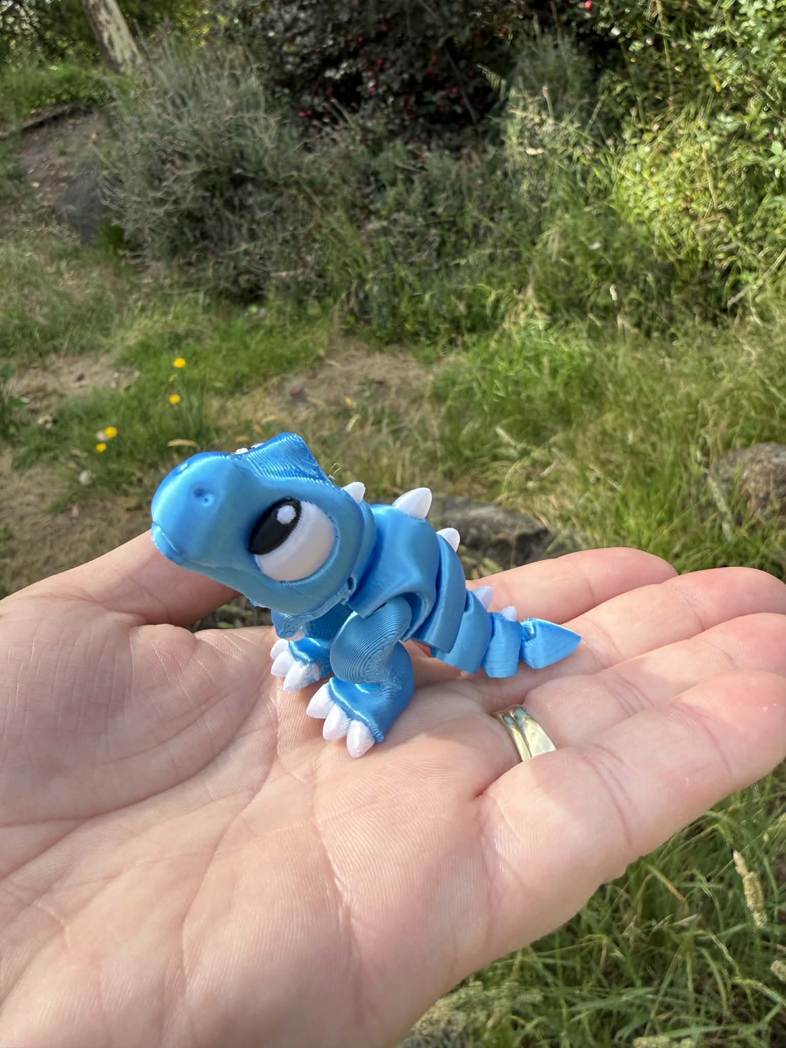 Blue 3D printed trex held in a hand with a natural background