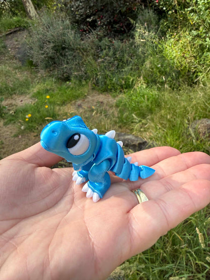 Blue 3D printed trex held in a hand with a natural background