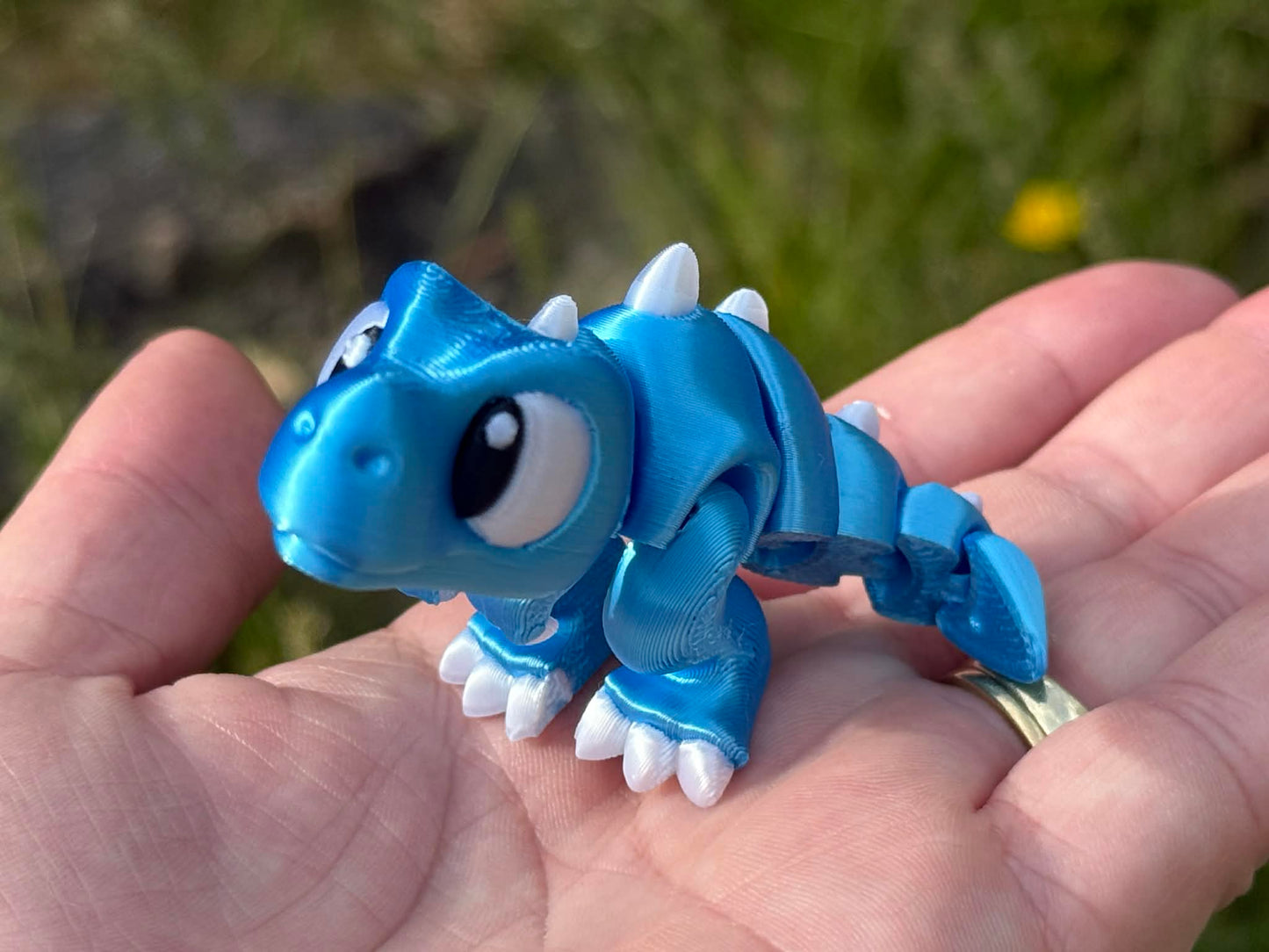 Blue 3d printed trex dinosaur held in a hand with a natural background