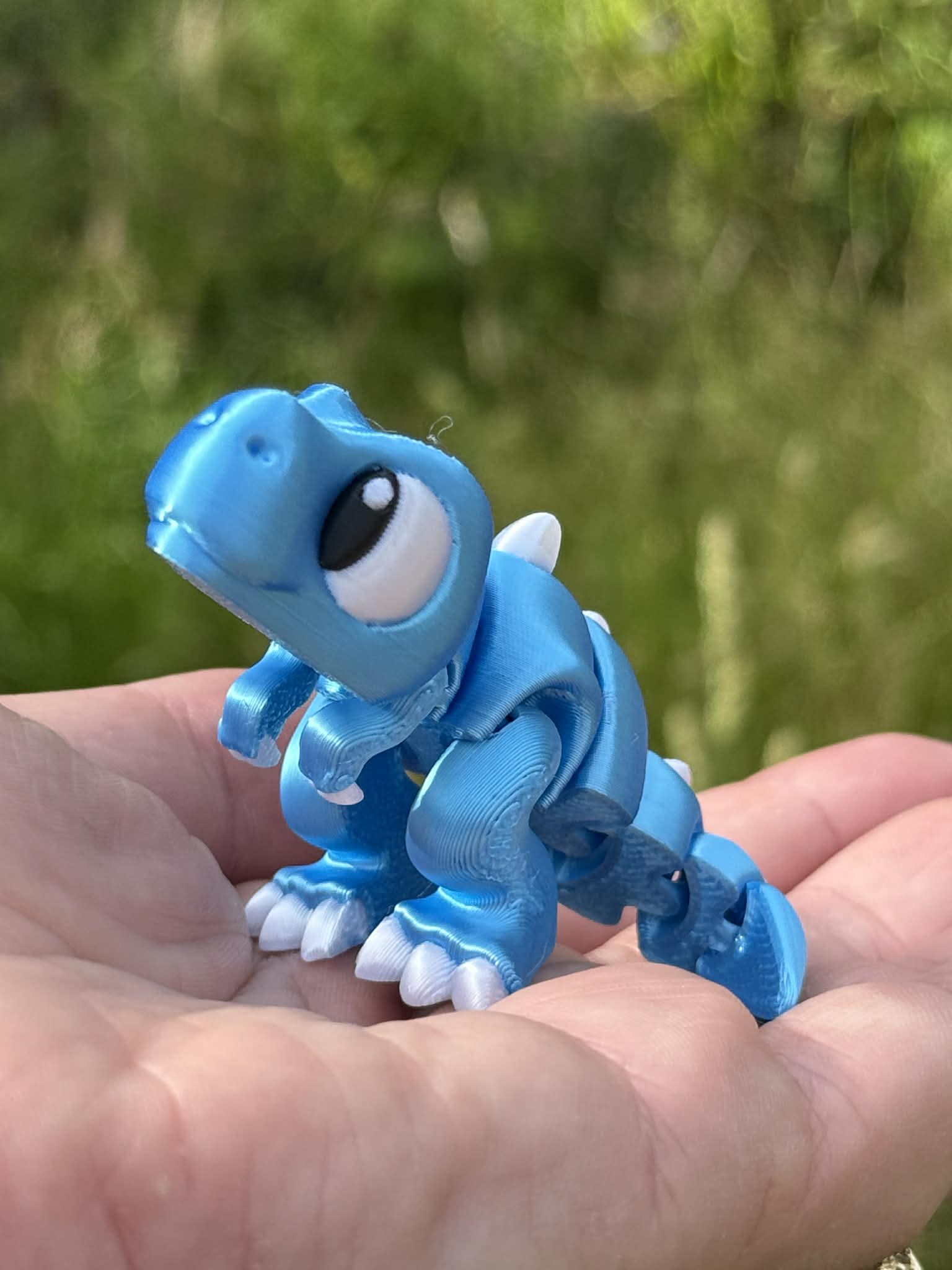Small blue dinosaur 3D printed held in a hand with a blurred green background