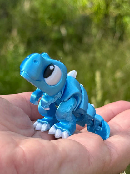 Small blue dinosaur 3D printed held in a hand with a blurred green background