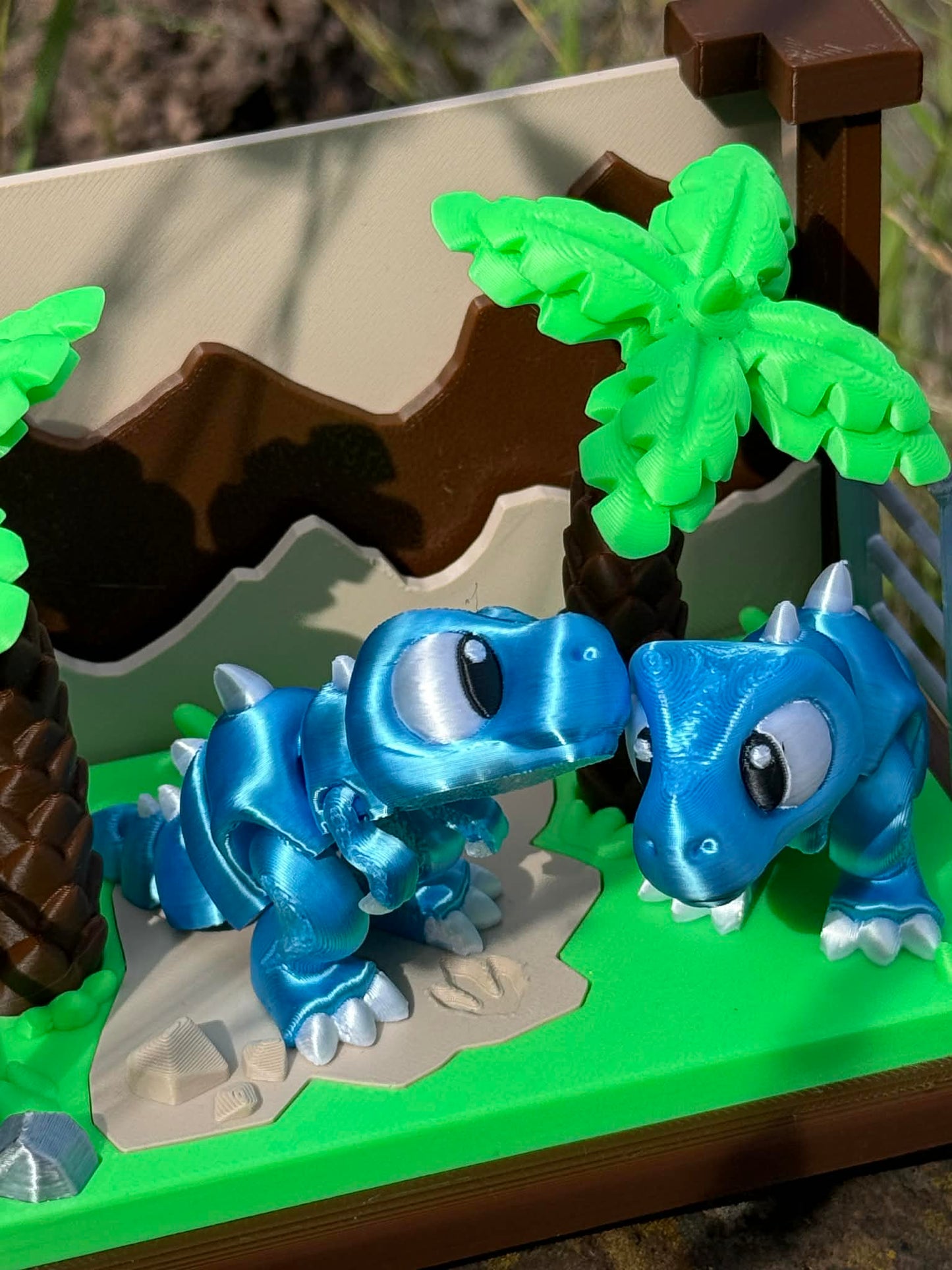 3D printed dinosaurs on a green base with a brown and beige landscape