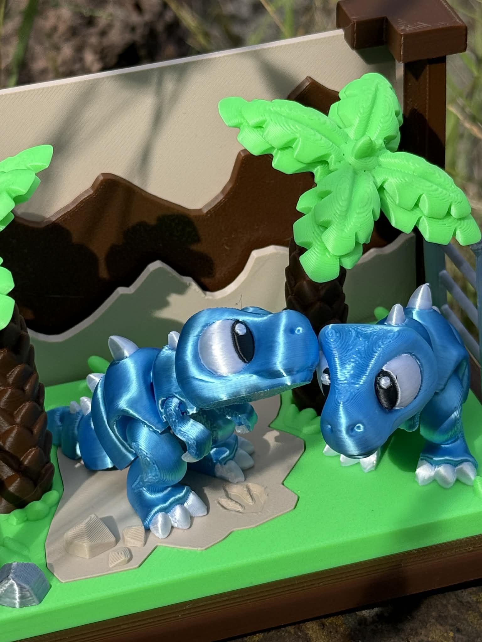 3D printed dinosaurs on a green base with a brown and beige landscape
