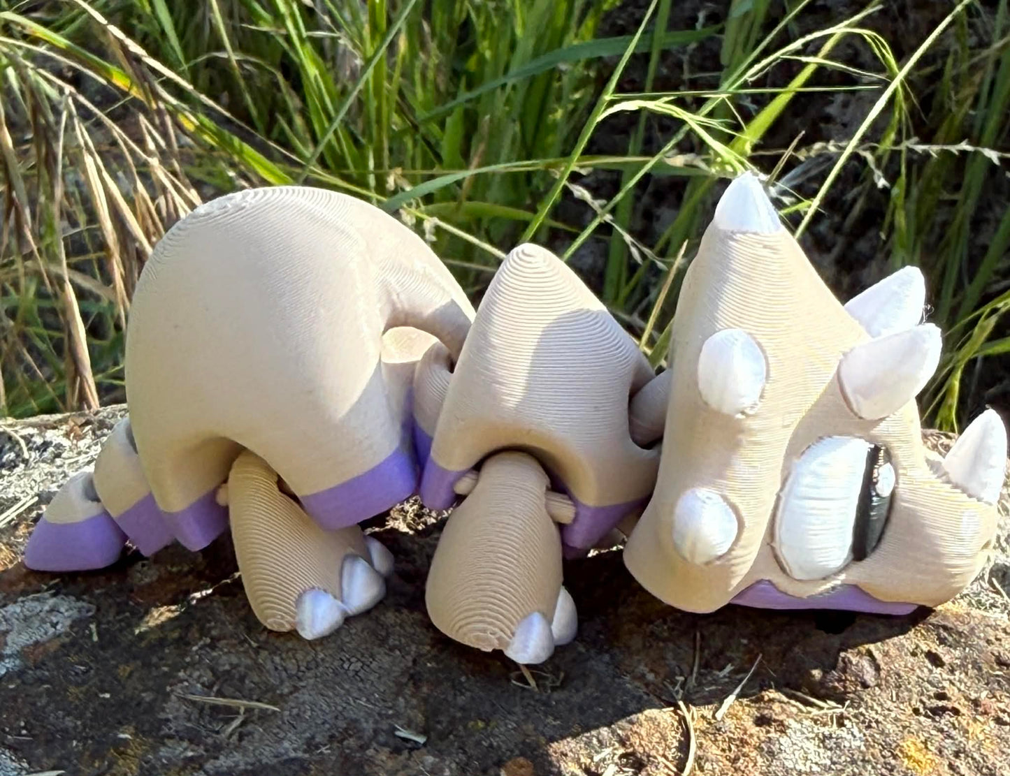 3d printed  triceratops on a stone surface with grass in the background