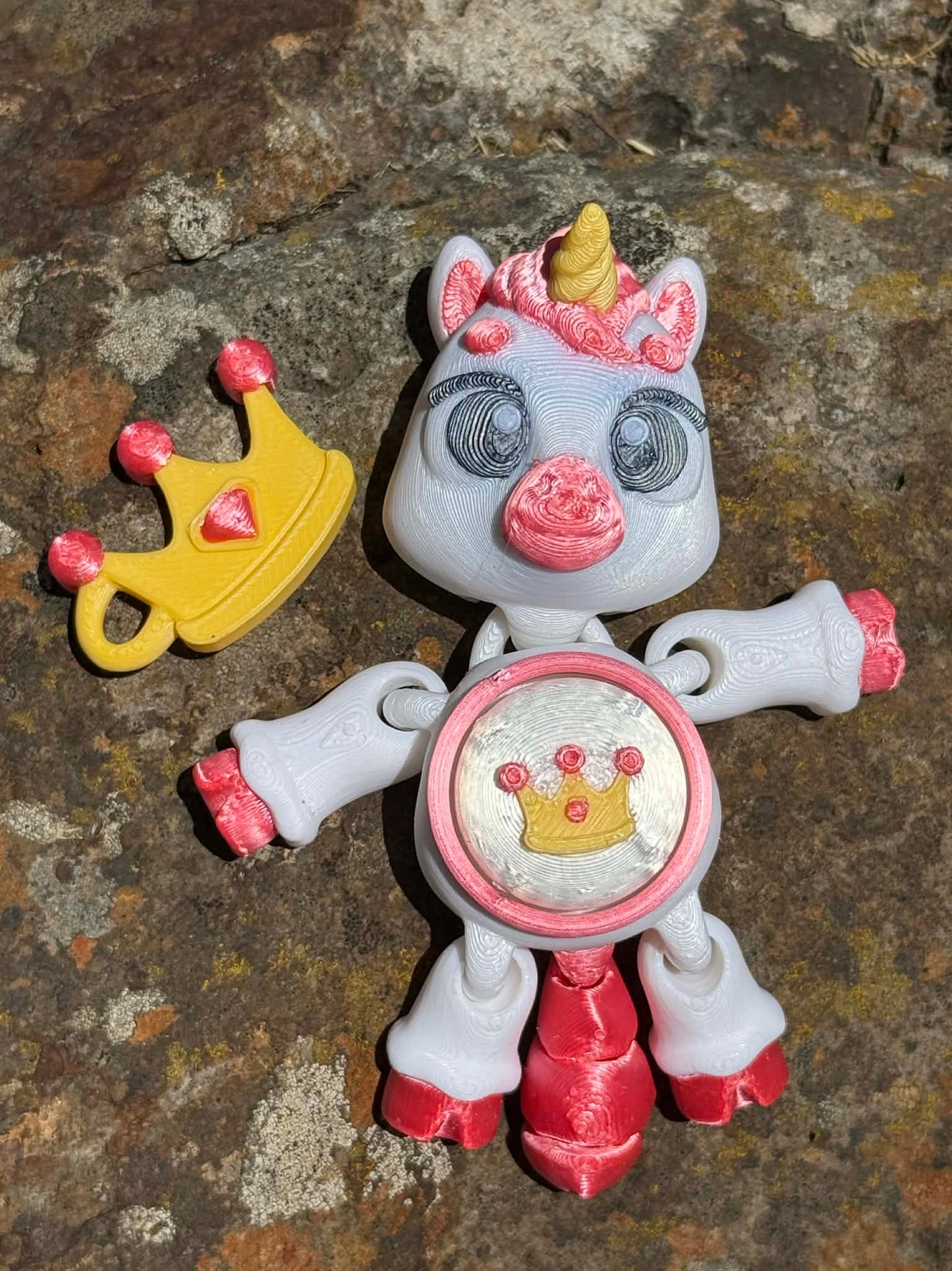 3D printed unicorn with a crown on its tummy and next to it on a stone surface