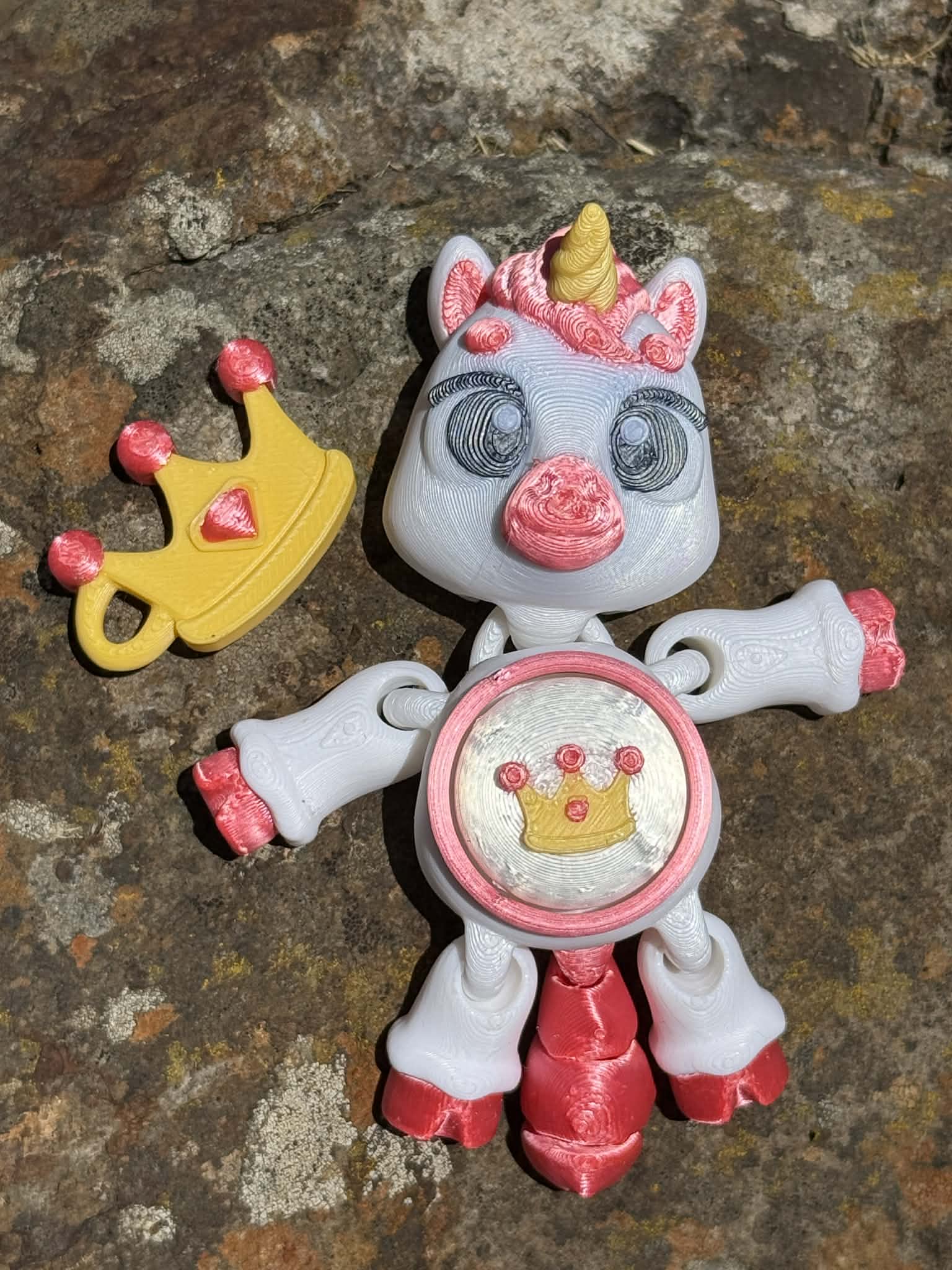 3D printed unicorn with a crown on its tummy and next to it on a stone surface