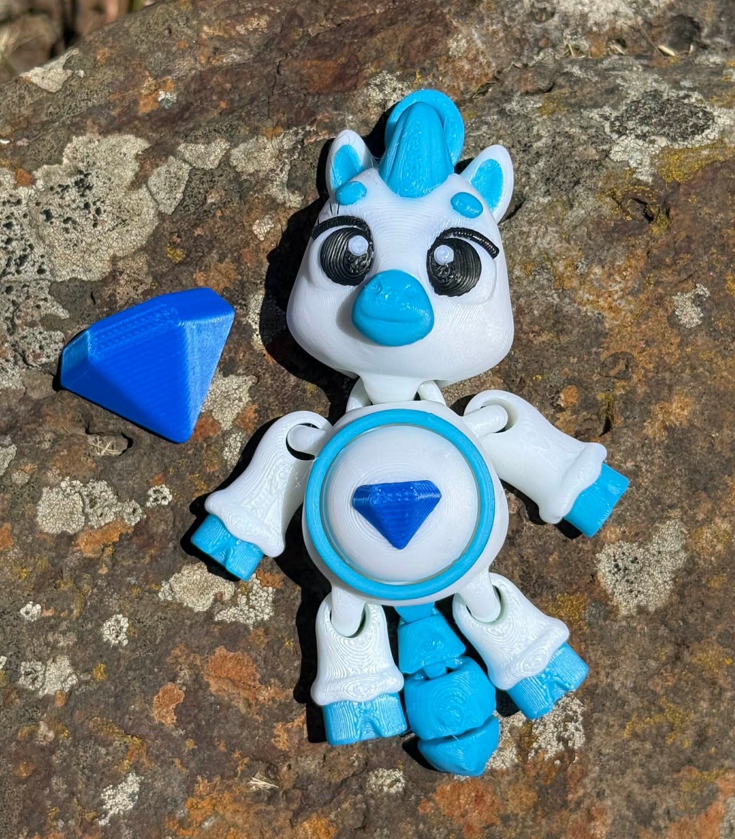 3D printed pony with blue and white design on a stone surface. with blue diamond on its tummy and next to it