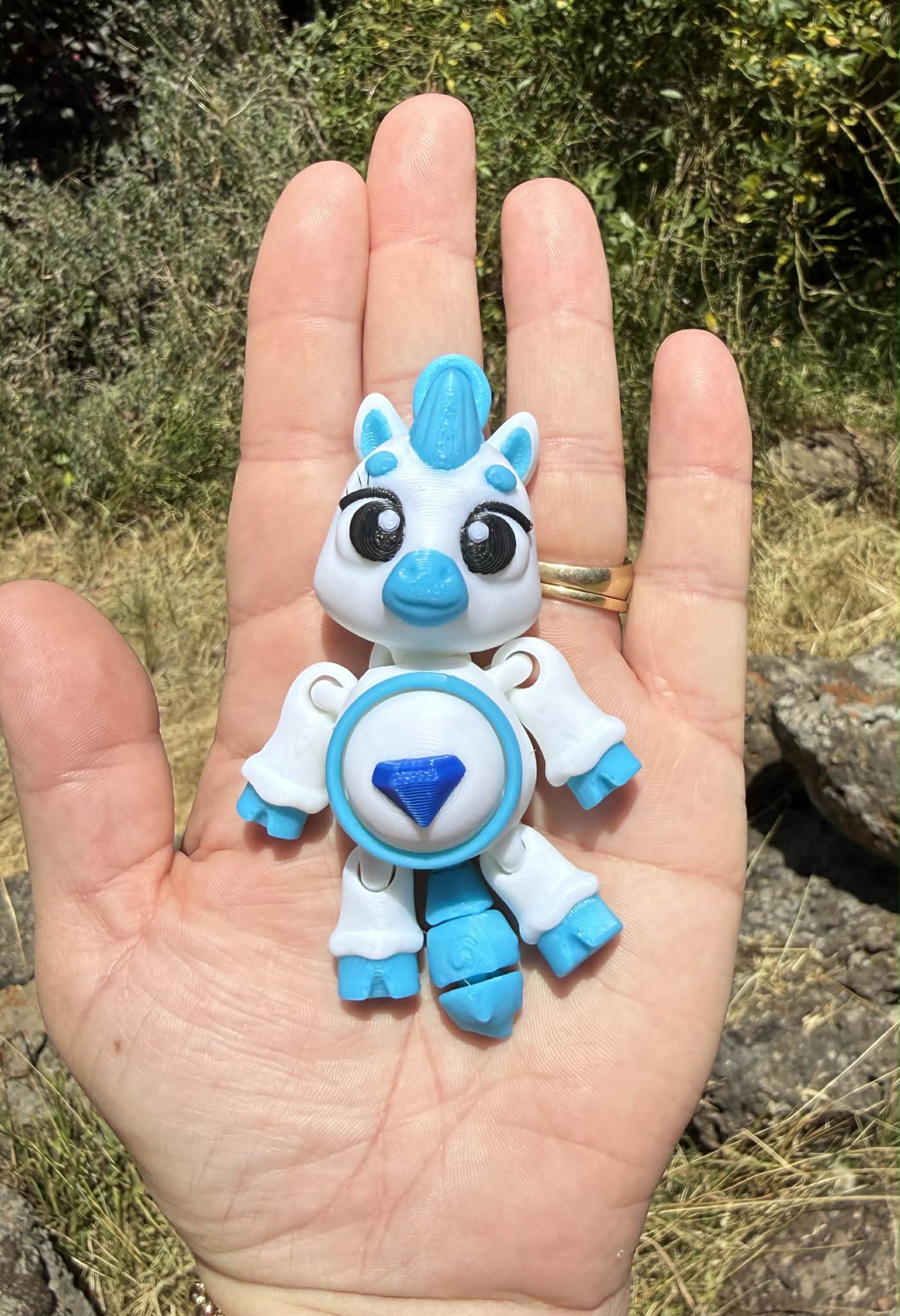 Small blue and white 3D printed pony held in a hand with a natural background