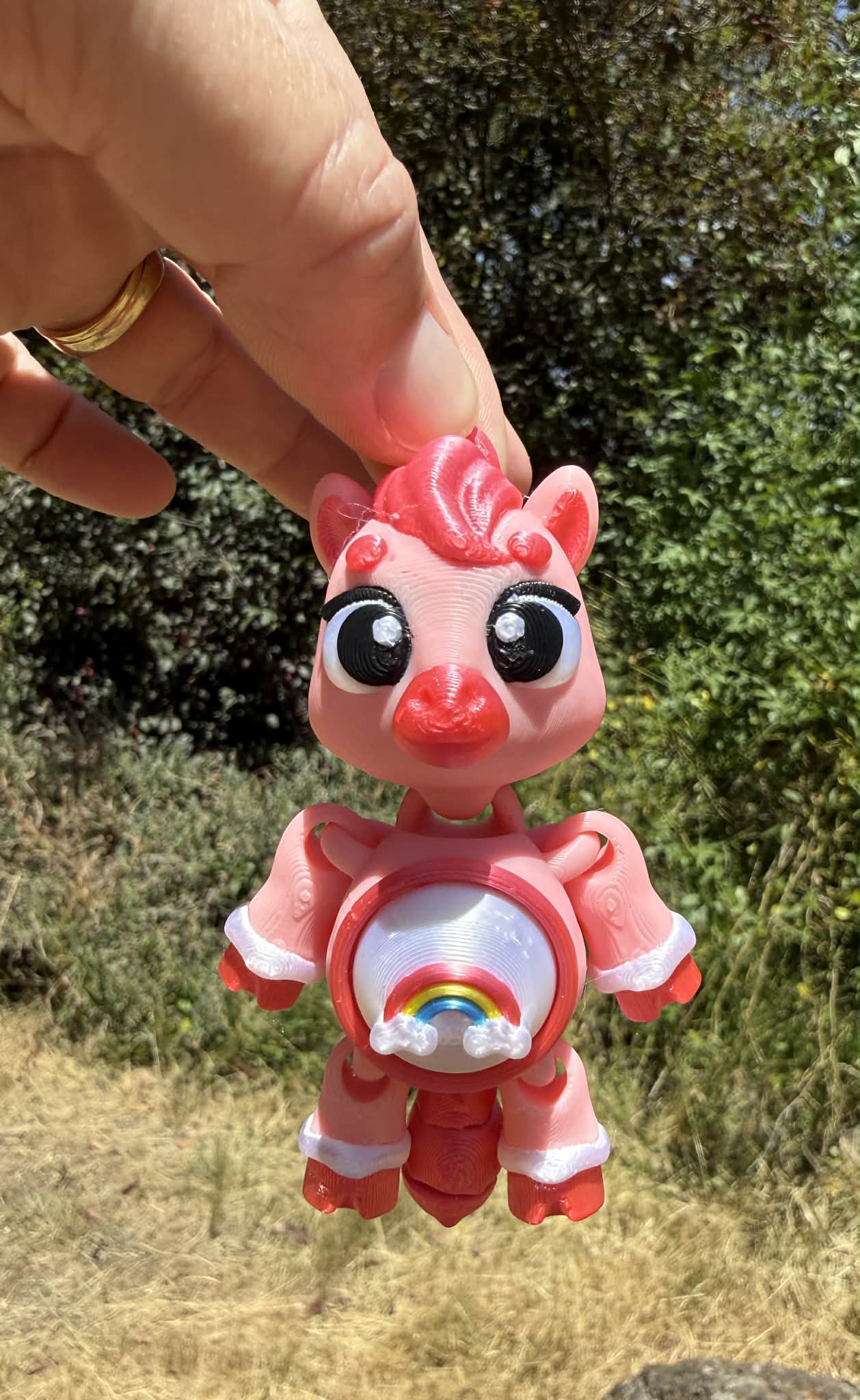 Small pink 3D printed pony with a rainbow on a tummy on a natural background. key ring model