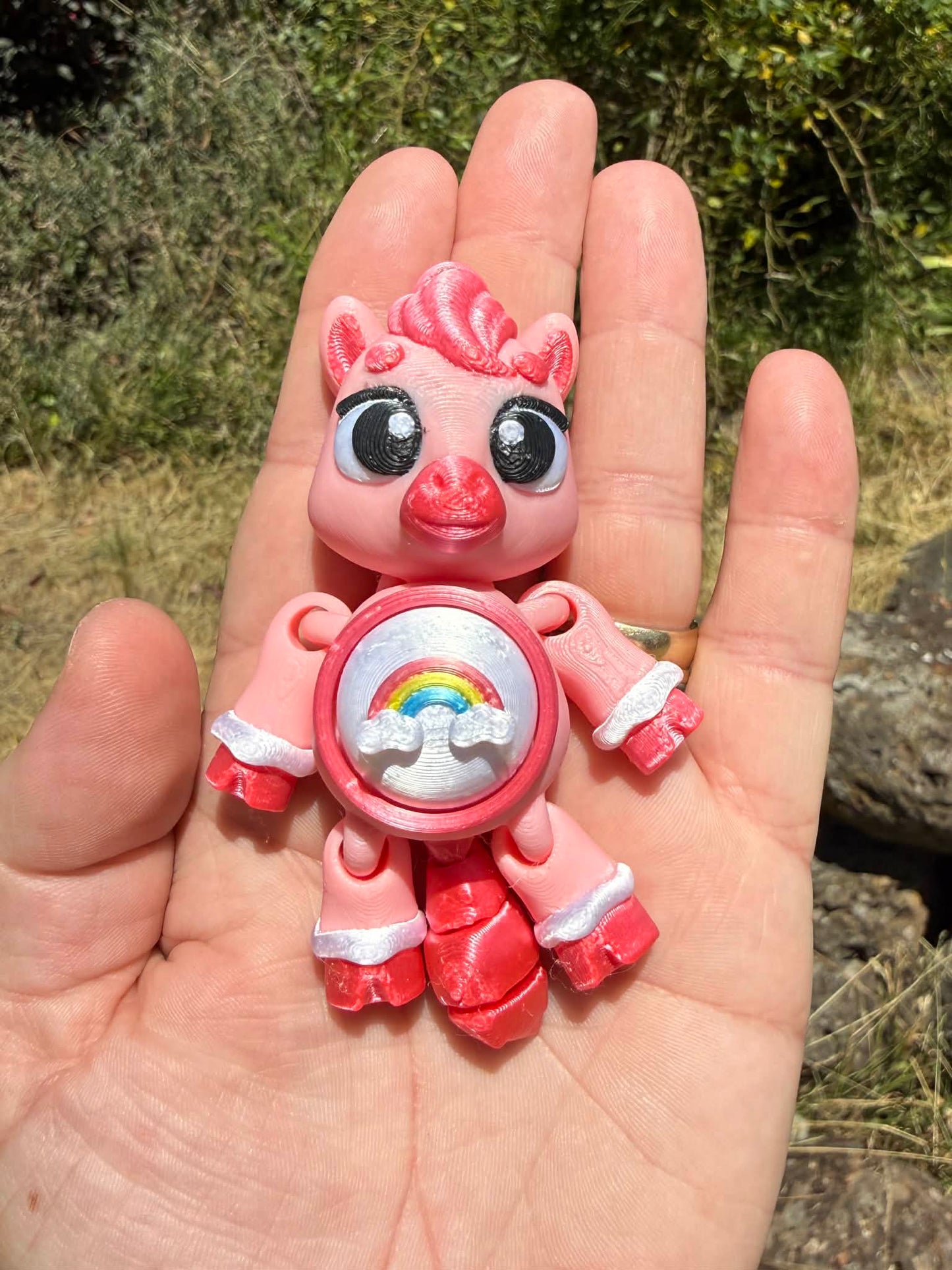 Pink pony 3D printed with a rainbow design on its tummy held in a hand against a natural background