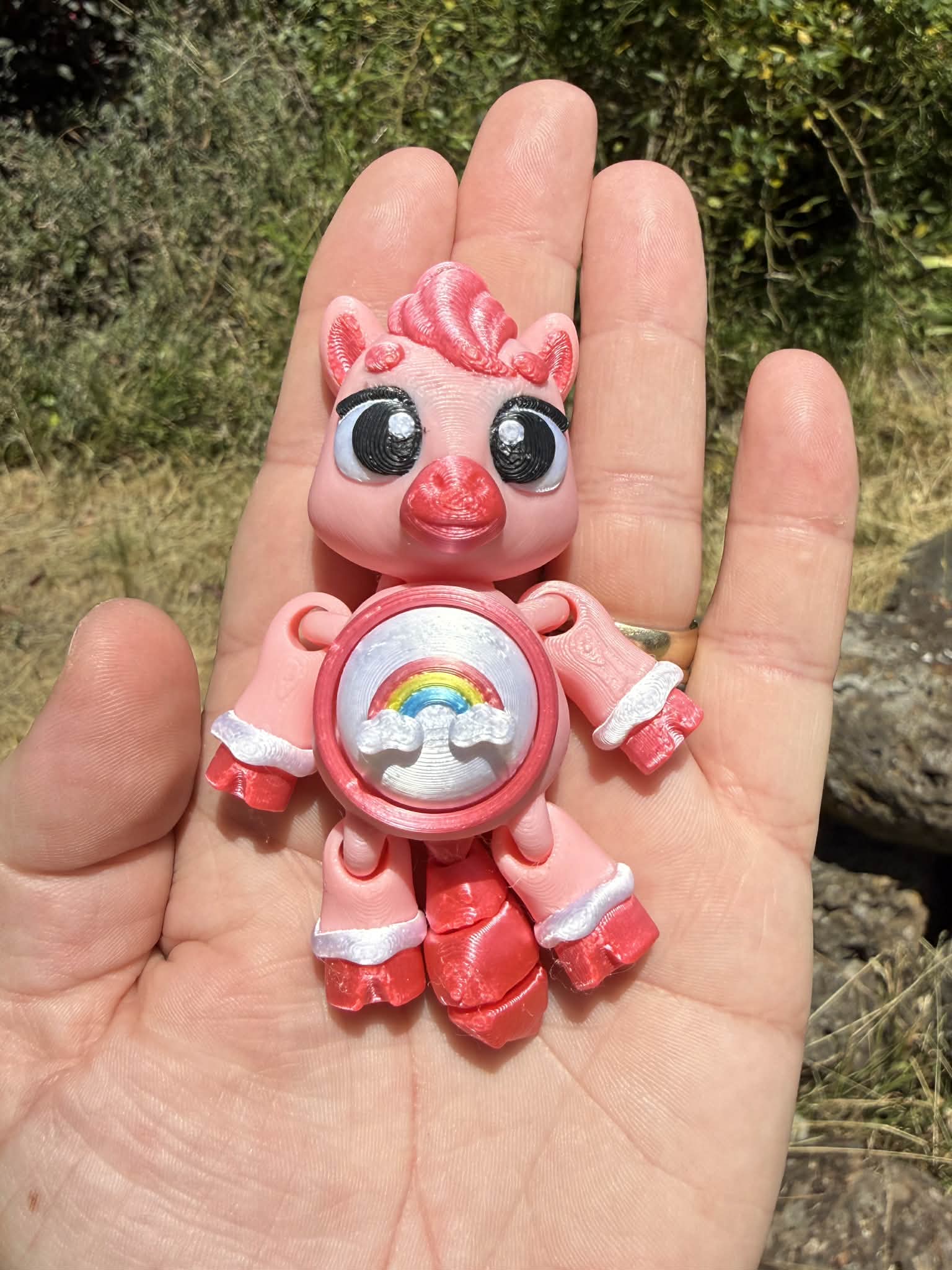 Pink pony 3D printed with a rainbow design on its tummy held in a hand against a natural background