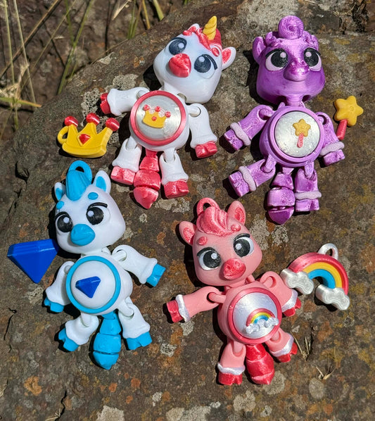 Four 3D printed colorful ponies and unicorn on a stone surface