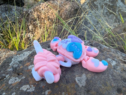 Pink and blue 3d printed turtle/highland cow on a rock with grass in the background