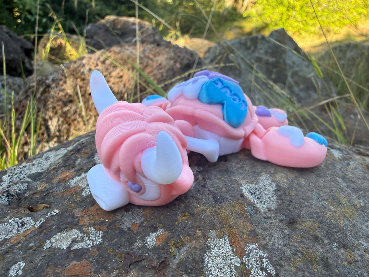 Pink and blue 3d printed turtle/highland cow on a rock with grass in the background