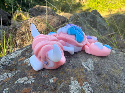 Pink and blue 3d printed turtle/highland cow on a rock with grass in the background