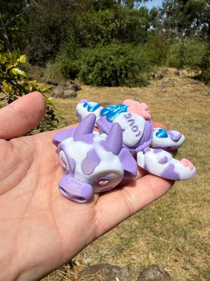 purple and blue 3d printed turtle/cow on a hand with grass in the background