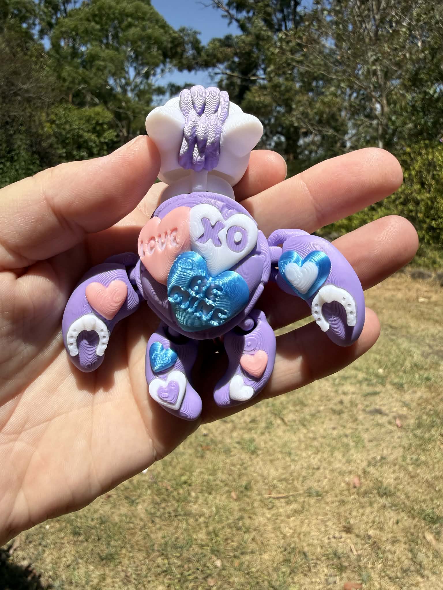 purple and blue 3d printed turtle/horse on a hand with grass in the background