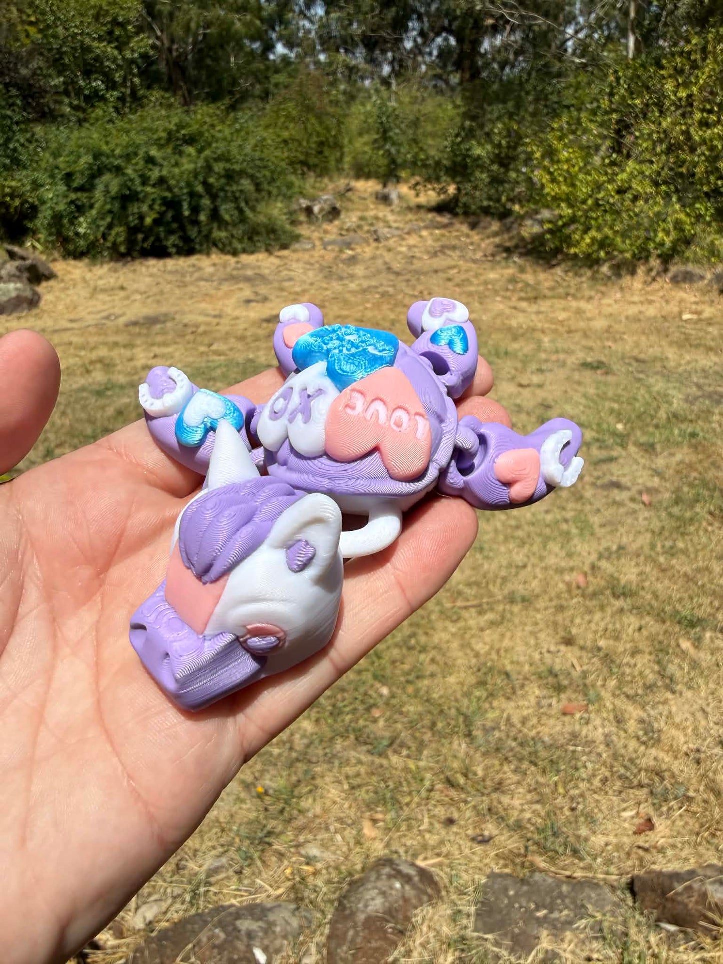 purple and blue 3d printed turtle/horse on a hand with grass in the background