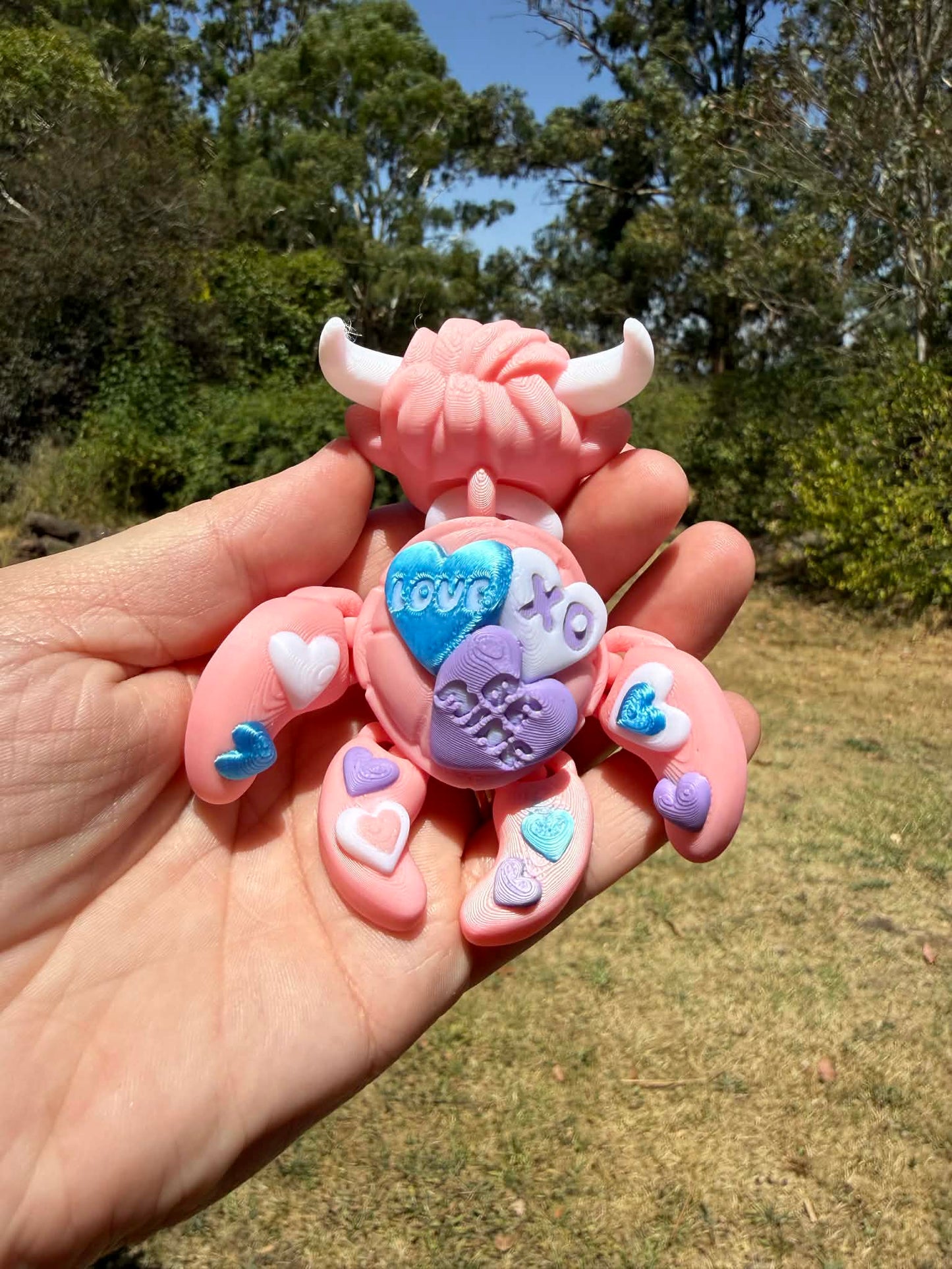 Pink and blue 3d printed turtle/highland cow on a rock with grass in the background
