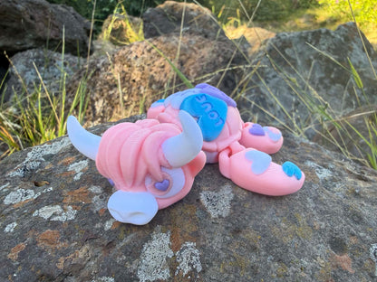 Pink and blue 3d printed turtle/highland cow on a rock with grass in the background