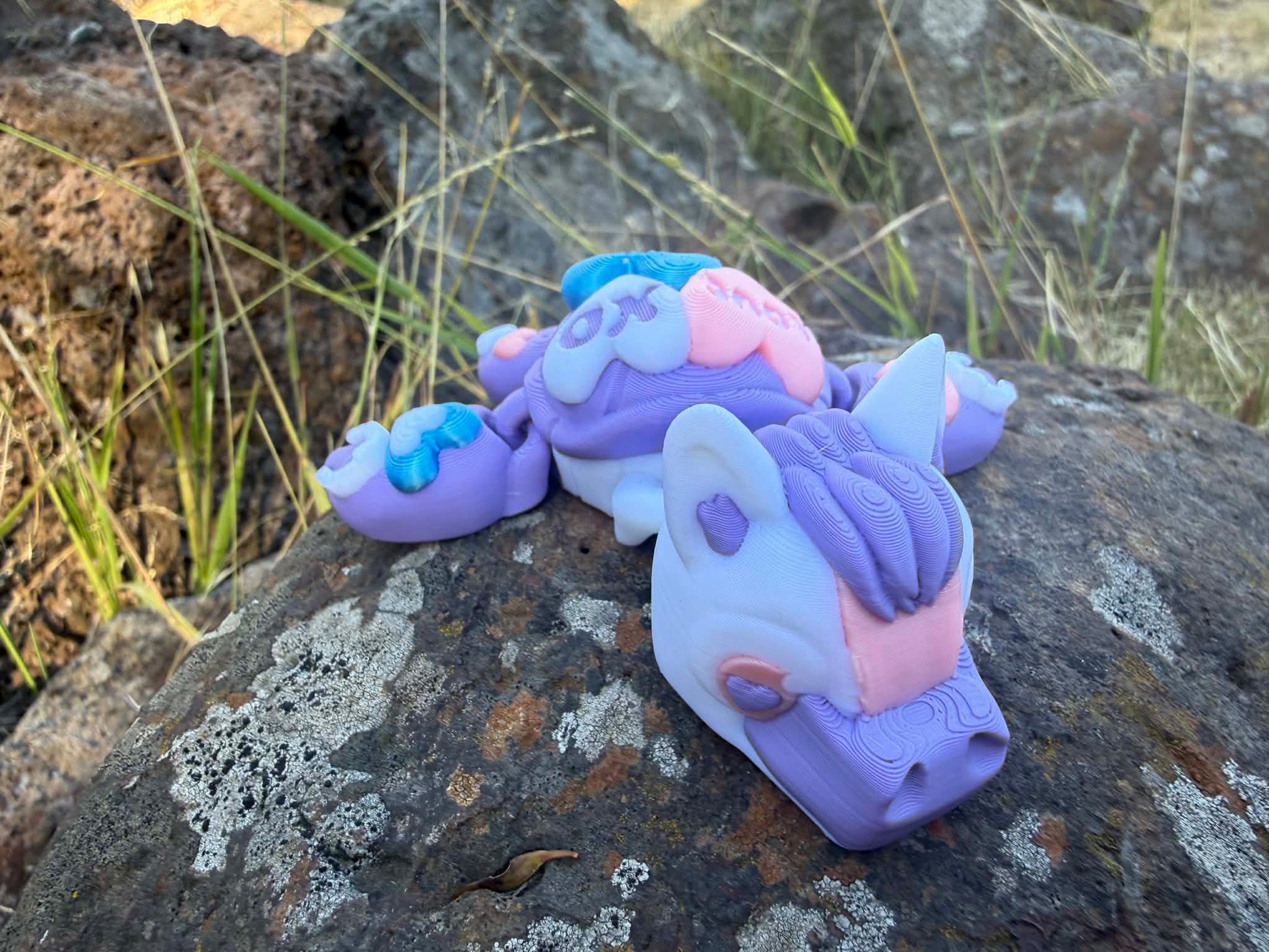 purple and blue 3d printed turtle/horse on a hand with grass in the background