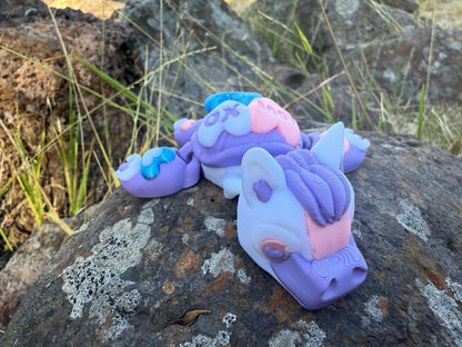 purple and blue 3d printed turtle/horse on a hand with grass in the background