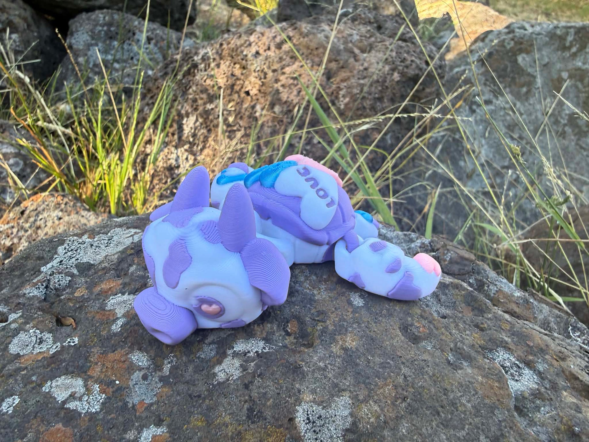 purple and blue 3d printed turtle/cow on a rock with grass in the background